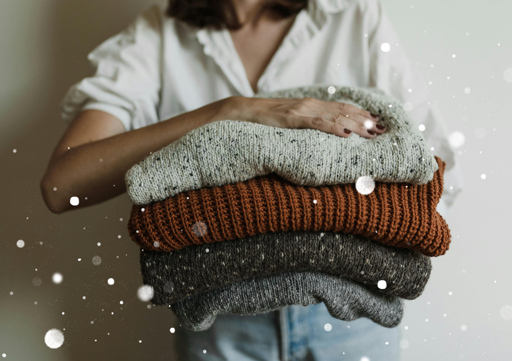 Person holding a stack of sweaters.